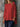 Person wearing a red shirt and dark pants against a stone wall