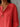 Person wearing a red shirt with a necklace against a gray wooden background