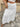Person wearing a white lace-trimmed skirt on a stone pavement