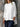 Person wearing a white oversized shirt and dark pants against a stone wall