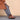 Person wearing brown Chelsea boots and a brown coat against a beige background
