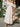 Woman in a beige off-shoulder dress holding a straw bag with flowers