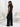 Woman in a black outfit holding a black handbag back view