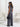 Woman in a gray jumpsuit holding a black handbag in a minimalistic room