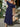Woman in a navy off-shoulder dress holding a straw bag with flowers, standing outdoors