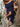 Woman in a navy off-shoulder dress with a floral bag, standing outdoors