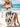 Woman in a white boho dress with blue patterns sitting on a beach