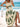 Woman in a white boho dress with green patterns sitting on a beach