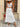 Woman in a white outfit with lace details standing in front of wooden shutters