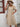 Woman wearing a beige dress and straw hat against a white wall