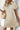 Woman wearing a beige dress holding a straw bag against a light background