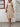 Woman wearing a beige dress standing against a white wall