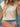 Woman wearing a beige top and denim shorts with a straw hat against a blue wooden background
