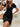 Woman wearing a black dress sitting on steps with a neutral background