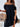 Woman wearing a black off-shoulder dress holding a woven handbag