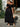 Woman wearing a black off-shoulder dress holding flowers outdoors