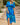Woman wearing a blue and green patterned dress standing on stone steps outdoors