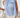 Woman wearing a blue and white striped sleeveless top with a bow detail, holding a beige handbag