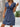 Woman wearing a blue dress with a wooden wall and plant in the background