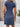 Woman wearing a blue dress standing against a wooden and white wall