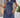 Woman wearing a blue dress with a wooden wall and plant in the background