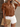 Woman wearing a brown ruffled blouse and white shorts, holding a straw bag against a neutral background