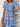 Woman wearing a colorful blue patterned dress with a white brick wall background