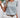 Woman wearing a floral top and white shorts with a straw hat, standing against a white wall