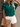 Woman wearing a green blouse, white shorts, and holding a straw bag against a neutral background