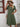 Woman wearing a green dress standing against a white wall
