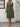 Woman wearing a green dress standing against a white wall