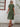 Woman wearing a green dress standing against a white wall, back view