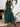 Woman wearing a green dress with black leaf pattern in a home setting