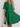 Woman wearing a green dress with ruffled details against a white wall