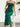 Woman wearing a green strapless dress with ruffles, sitting on a white stool