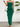 Woman wearing a green strapless ruffled dress with a white wall and plant in the background
