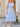 Woman wearing a light blue dress standing outdoors near a wooden door