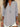 Woman wearing a light gray long-sleeve top with a blurred background