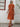 Woman wearing a orange-colored dress and straw hat against a white wall