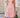 Woman wearing a pink dress standing outdoors on a stone patio
