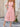 Woman wearing a pink dress standing outdoors on a stone patio