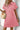 Woman wearing a pink dress with a textured pattern against a white wall