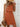 Woman wearing a rust-colored dress with a straw hat and brown bag against a light background