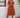 Woman wearing a rust-colored dress with a straw hat and sunglasses, standing against a white wall