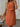 Woman wearing a rust-colored dress with a textured pattern, standing outdoors