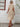 Woman wearing a tan dress standing against a white wall