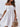 Woman wearing a white off-shoulder dress holding a wicker bag against a light background