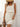 Woman wearing a white sleeveless dress with a straw hat and holding a brown bag against a light background