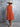 Woman wearing an orange dress and wide-brimmed hat against a gray wall