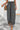 Woman wearing black and white patterned wide-leg pants with a white top and brown sandals, standing on a concrete floor